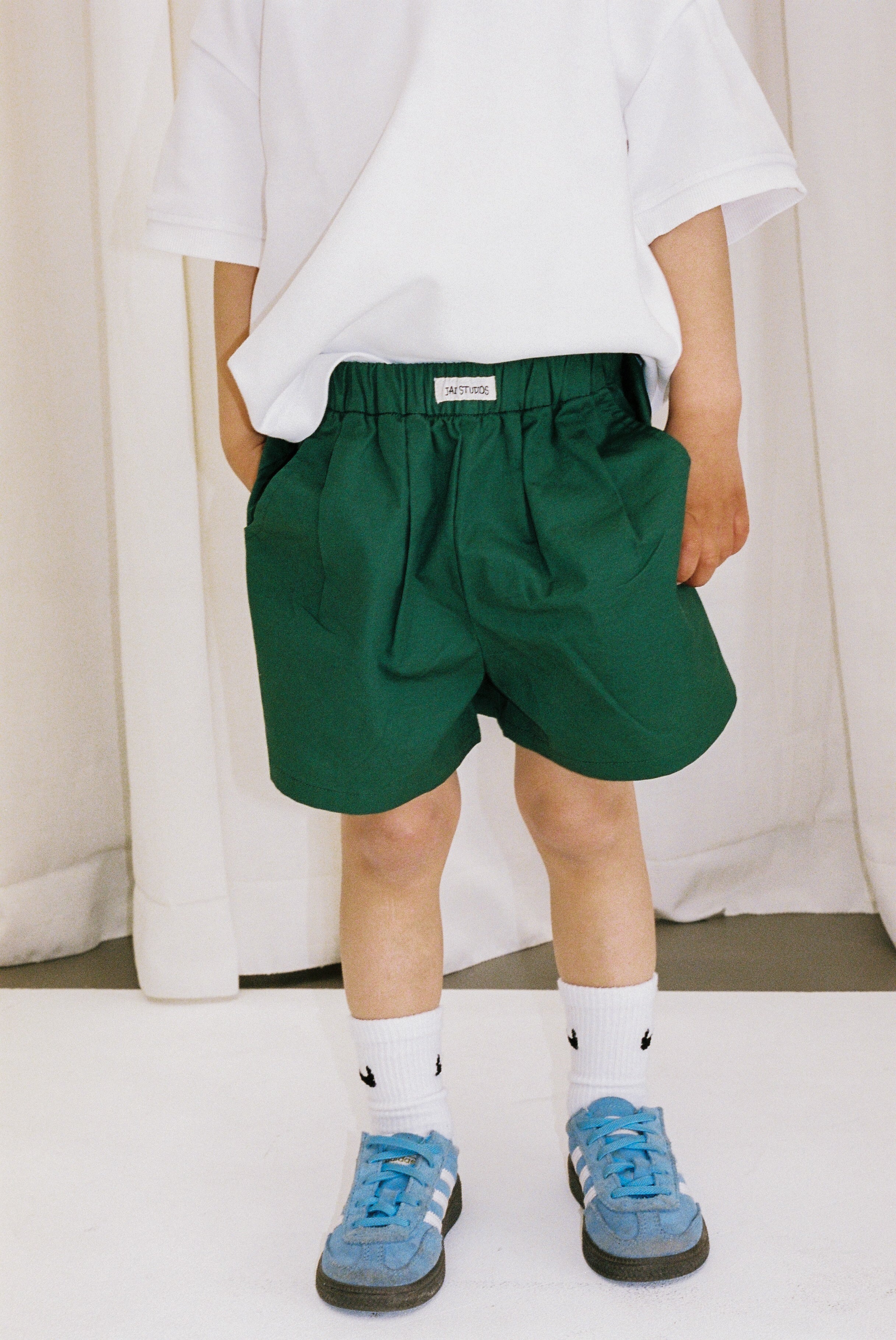 Jai Studios Forest Shorts in green fabric with side pockets, displayed on a hanger against a neutral background