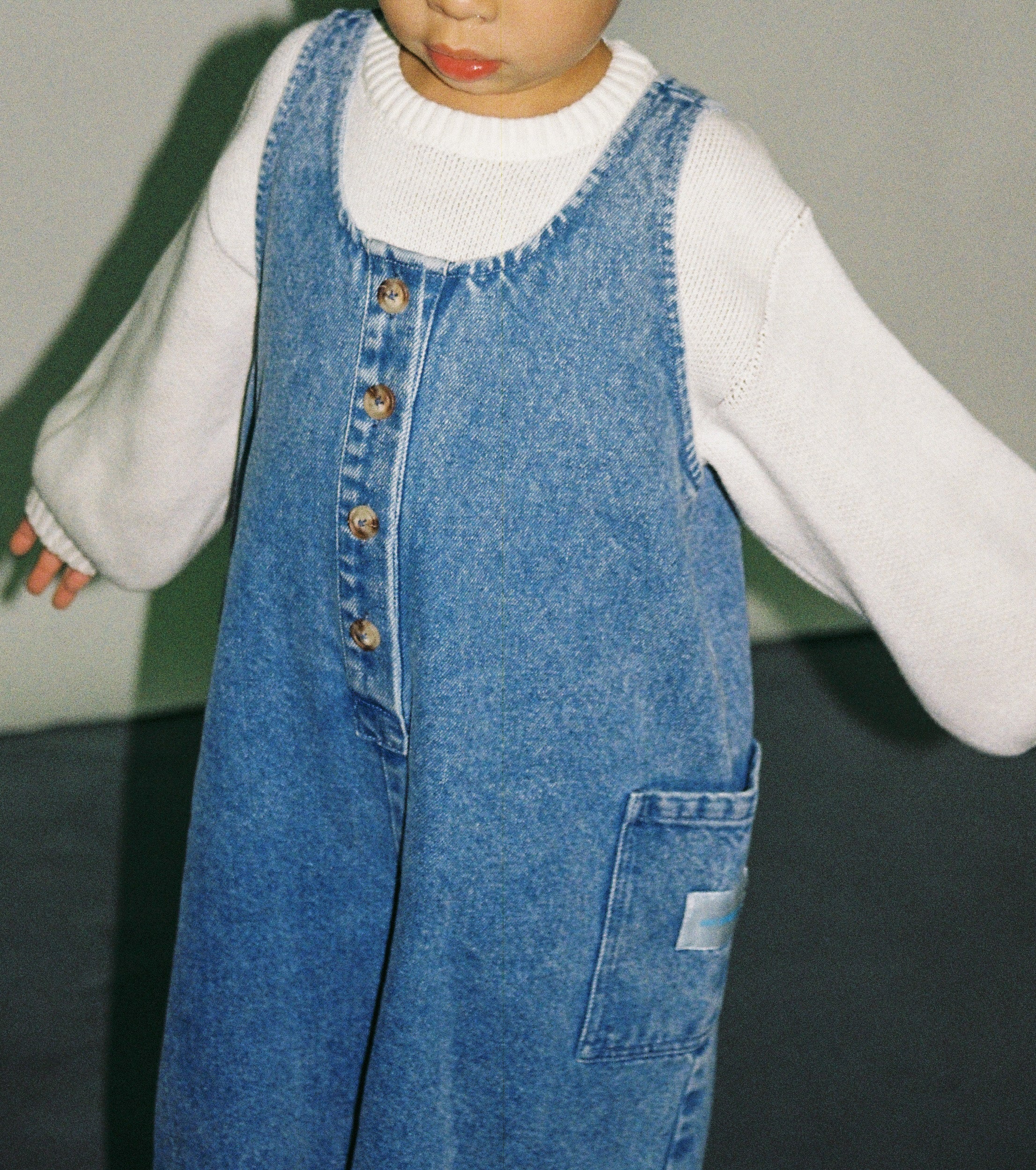 Kid wearing blue denim overalls over a white sweater