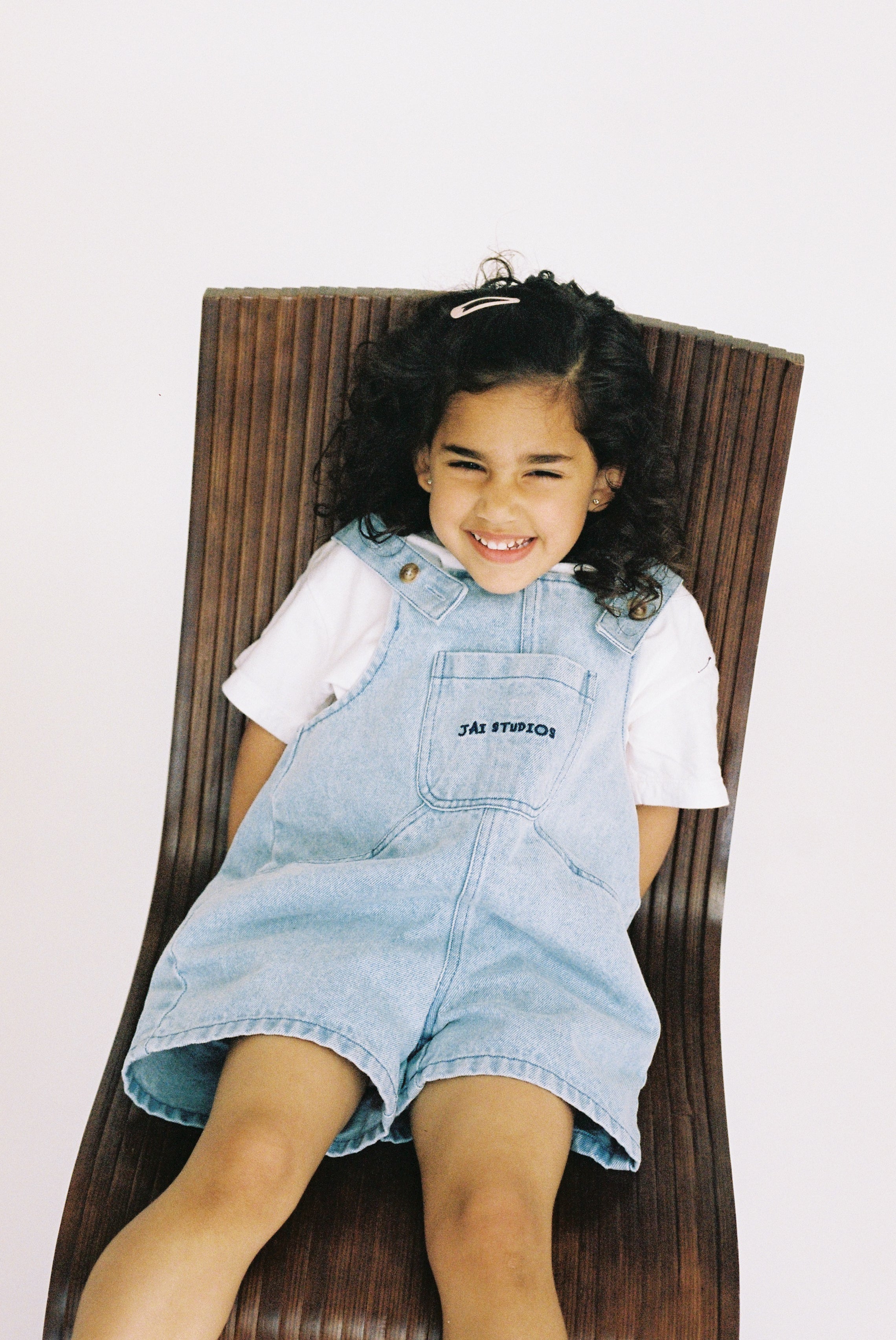 Jai Studios Lux Overalls in neutral fabric, featuring adjustable straps and front pockets, displayed on a hanger.